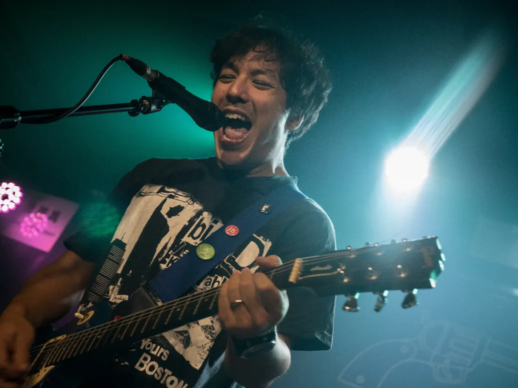 Wai Lee shouting into a microphone while playing guitar